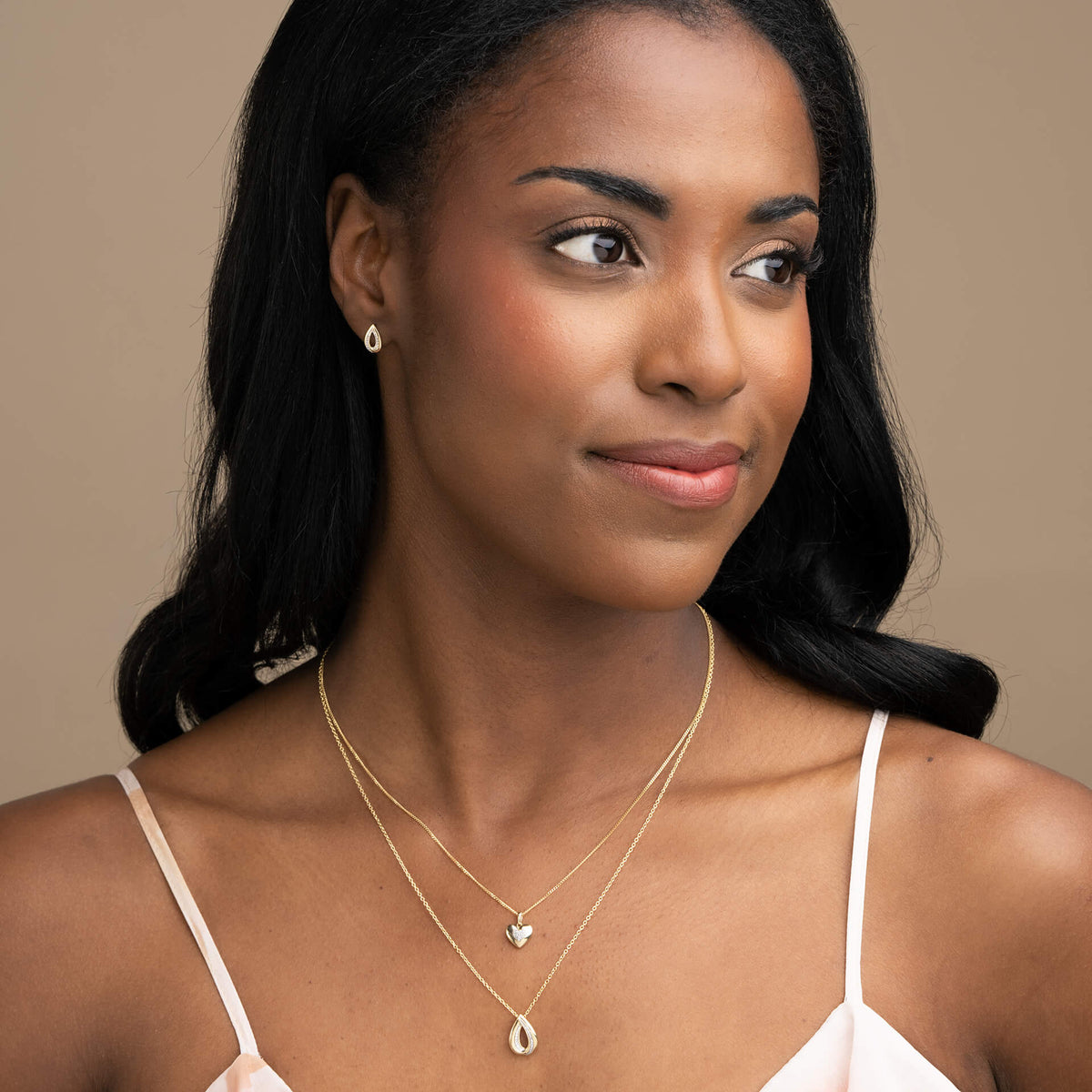 woman wearing Gold Cut Out Diamond Teardrop Pendant necklace and earrings on ear set with heart necklace layering around neck