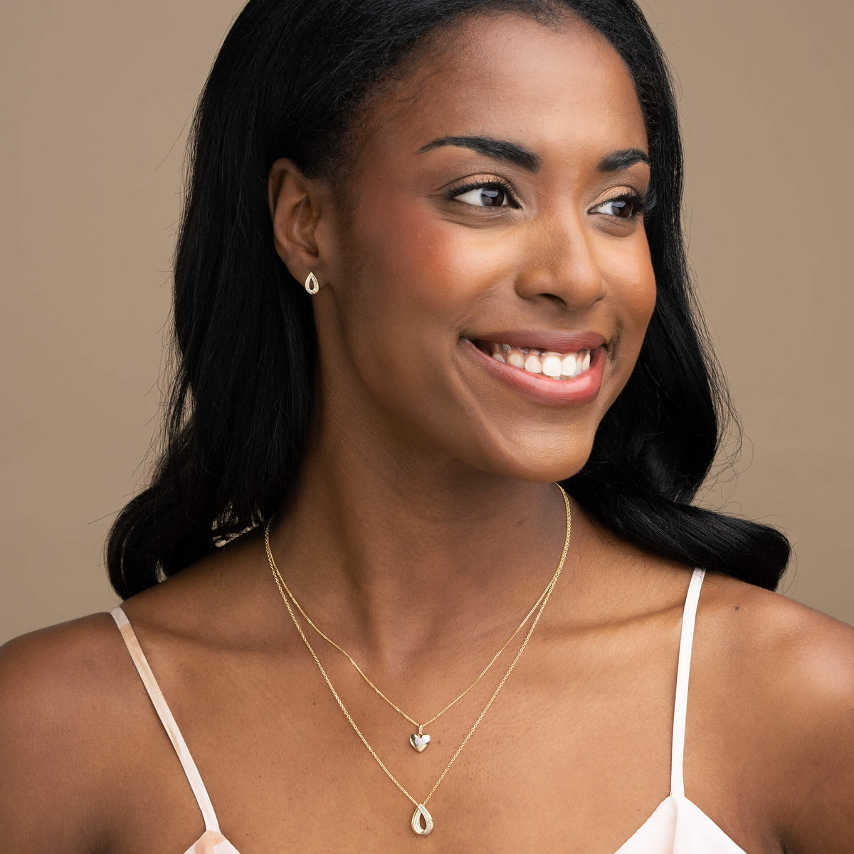 woman wearing Gold Cut Out Diamond Teardrop Pendant necklace and earrings on ear set with heart necklace layering around neck
