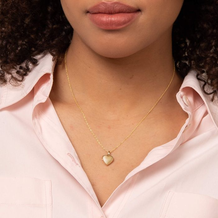 Close-up of a person wearing woman wearing Stippled Bale Gold Heart Locket Necklace, set against a blurred background.