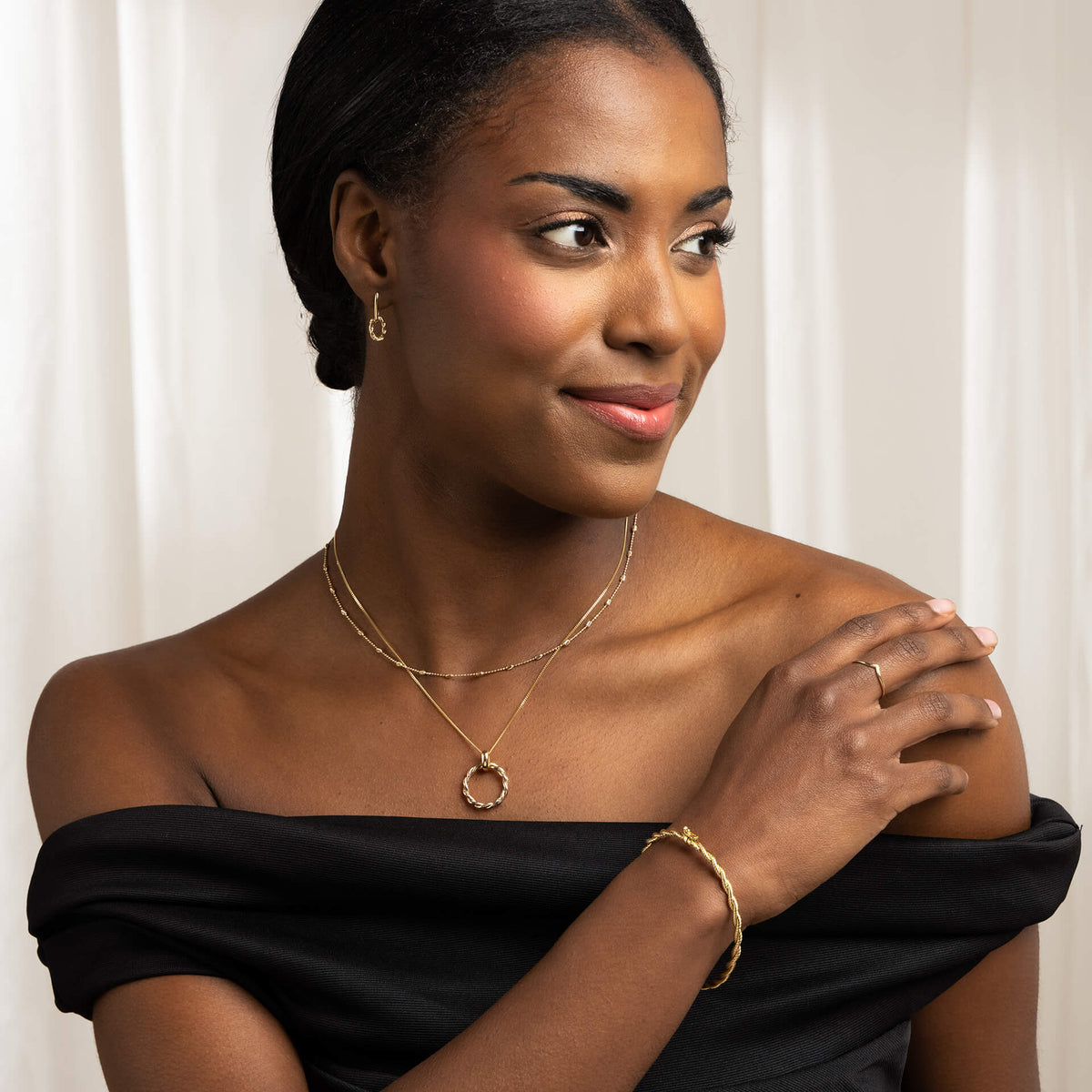 woman wearing twisted gold bangle gold rope earring and necklace layered with another chain 