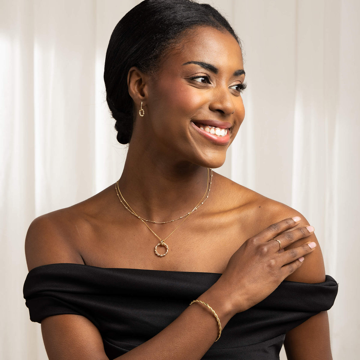 woman wearing twisted gold bangle gold rope earring and necklace layered with another chain smiling